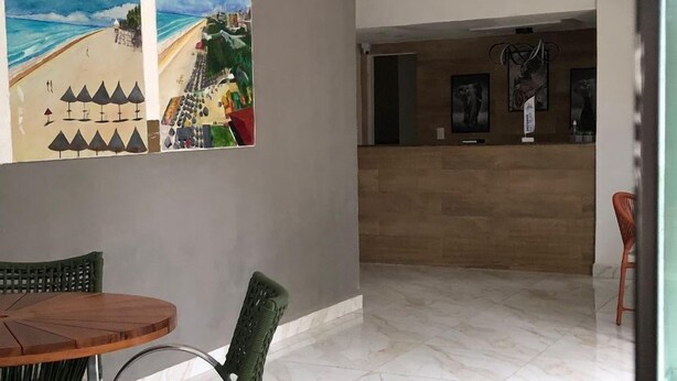 A reception area with a reception desk, a seating area with a table and chairs, and a large painting on the wall. - Pousada Toco do Mar (Fortaleza)