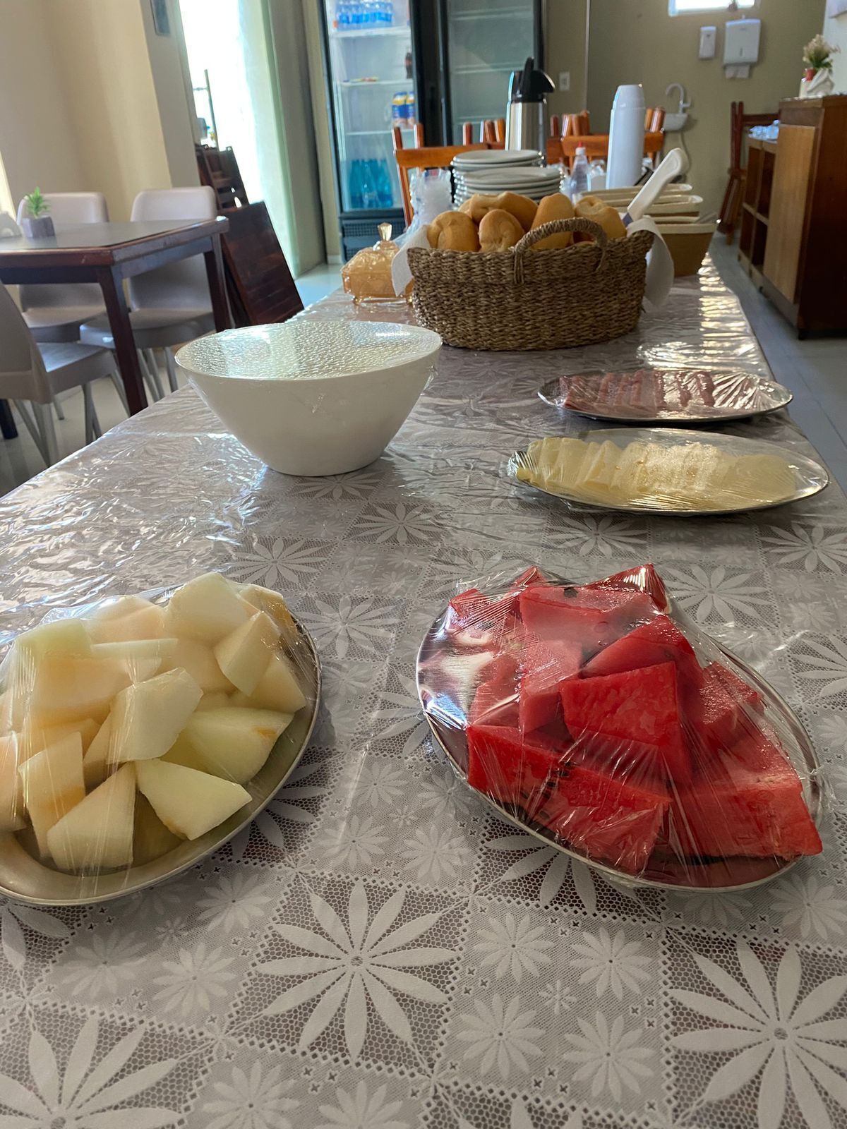 A table with various food items, including a bowl of white cheese, a plate of red fruit, and a basket of bread.