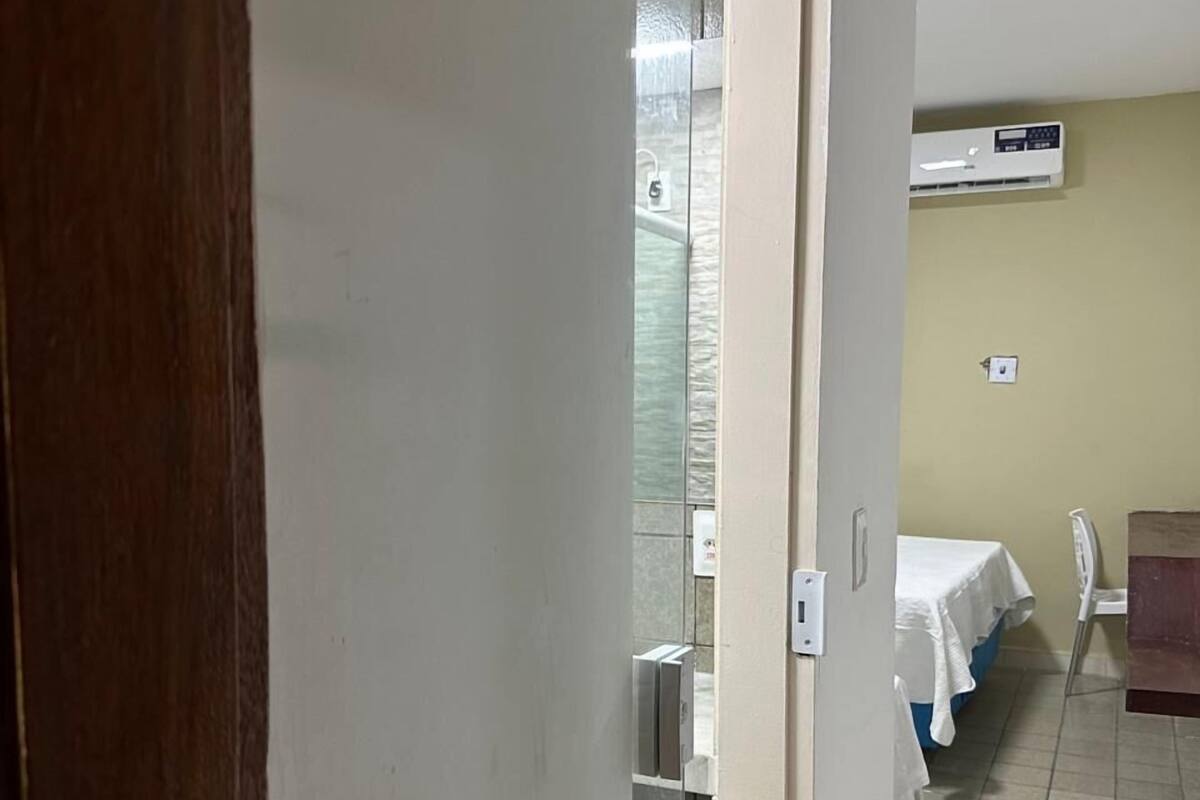 A hotel room with a bed, a small table, and a chair. There is a window with a view of the outside.