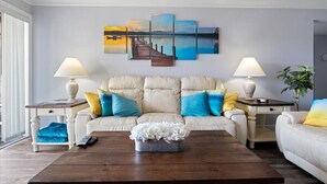 A living room with a beige sofa, two side tables with lamps, a coffee table with a flower arrangement, and a large landscape painting on the wall. - Lake View Condo - Heart of Osage Beach + Boat Slip (Osage Beach)