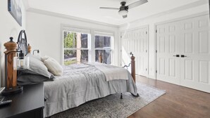 A bedroom with a bed, a desk, a chair, a ceiling fan, and a view of the outdoors through large windows. - The Alpine Estate At Copper Chase (Brian Head)