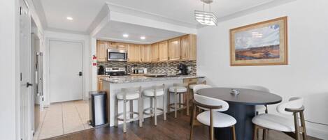 A modern kitchen with wooden cabinets, a central island with bar stools, and a dining table with chairs.