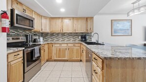 A modern kitchen with wooden cabinets, a granite countertop, and a tiled backsplash. - The Alpine Estate At Copper Chase (Brian Head)