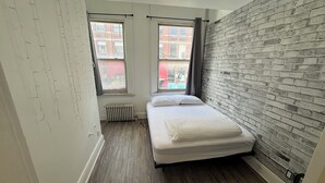 A small, modern bedroom with a brick wall, a single bed, two windows with curtains, and a radiator. - Beautiful apartment on Richmond near via rail (London)
