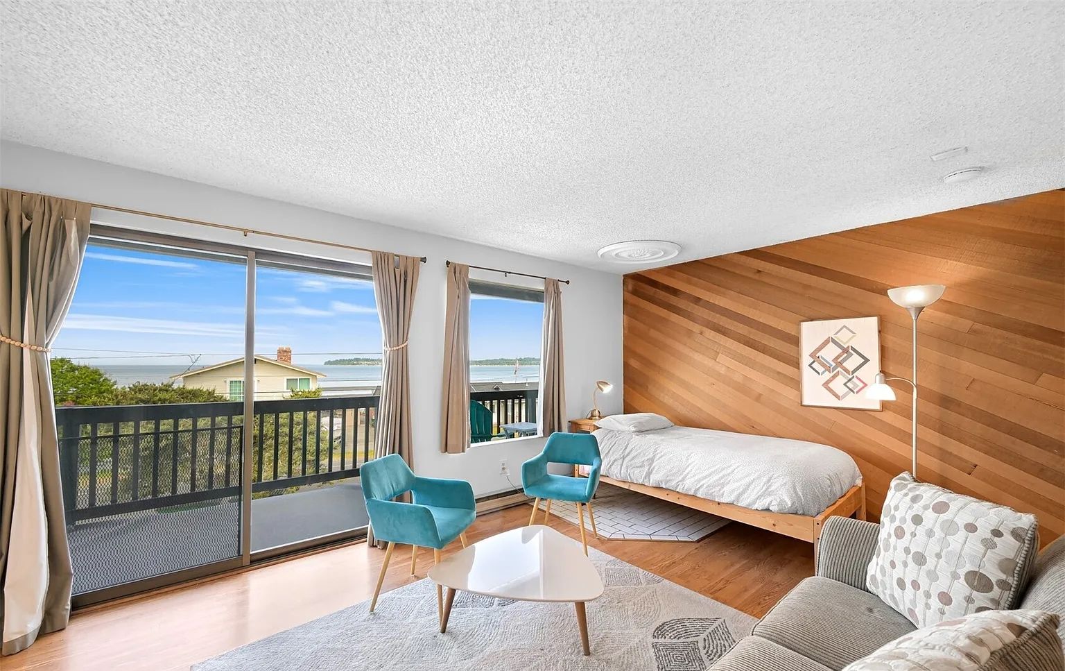 A modern bedroom with a bed, a sofa, a chair, and a view of the sea.
