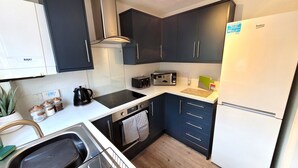 A compact kitchen with dark cabinets, a Baxi coffee machine, a toaster, and a refrigerator.