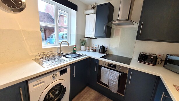 A compact kitchen with a washing machine, a sink, a stove, and a toaster.