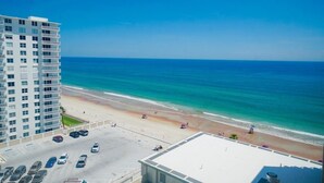 A high-rise hotel overlooking a beach with a parking lot and a clear view of the ocean.