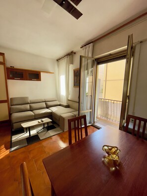 A living room with a sofa, a dining table, and a view through a glass door. - Apartment Mestre Venice (Venezia)