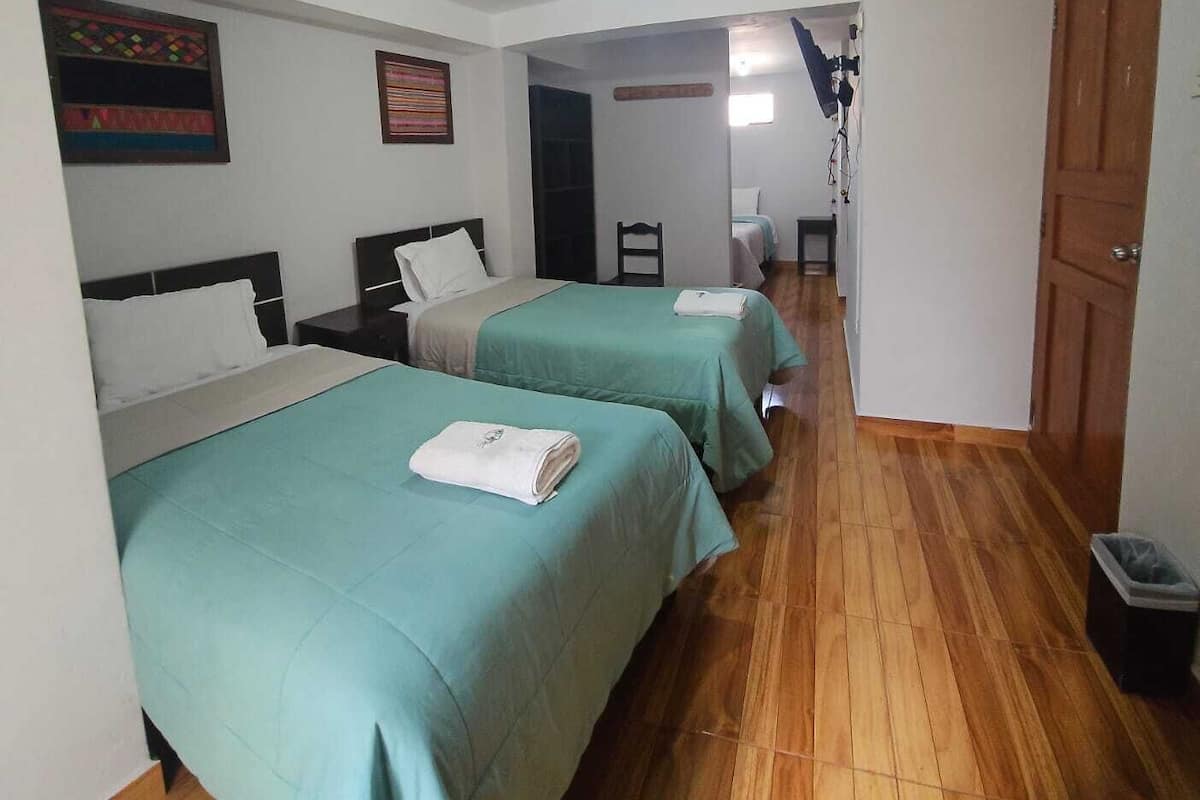 A hotel room with two beds, a wooden floor, a door, and a small trash bin.