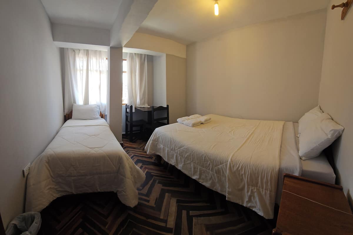 A bedroom with two beds, a wooden floor, a desk, and a window with curtains.