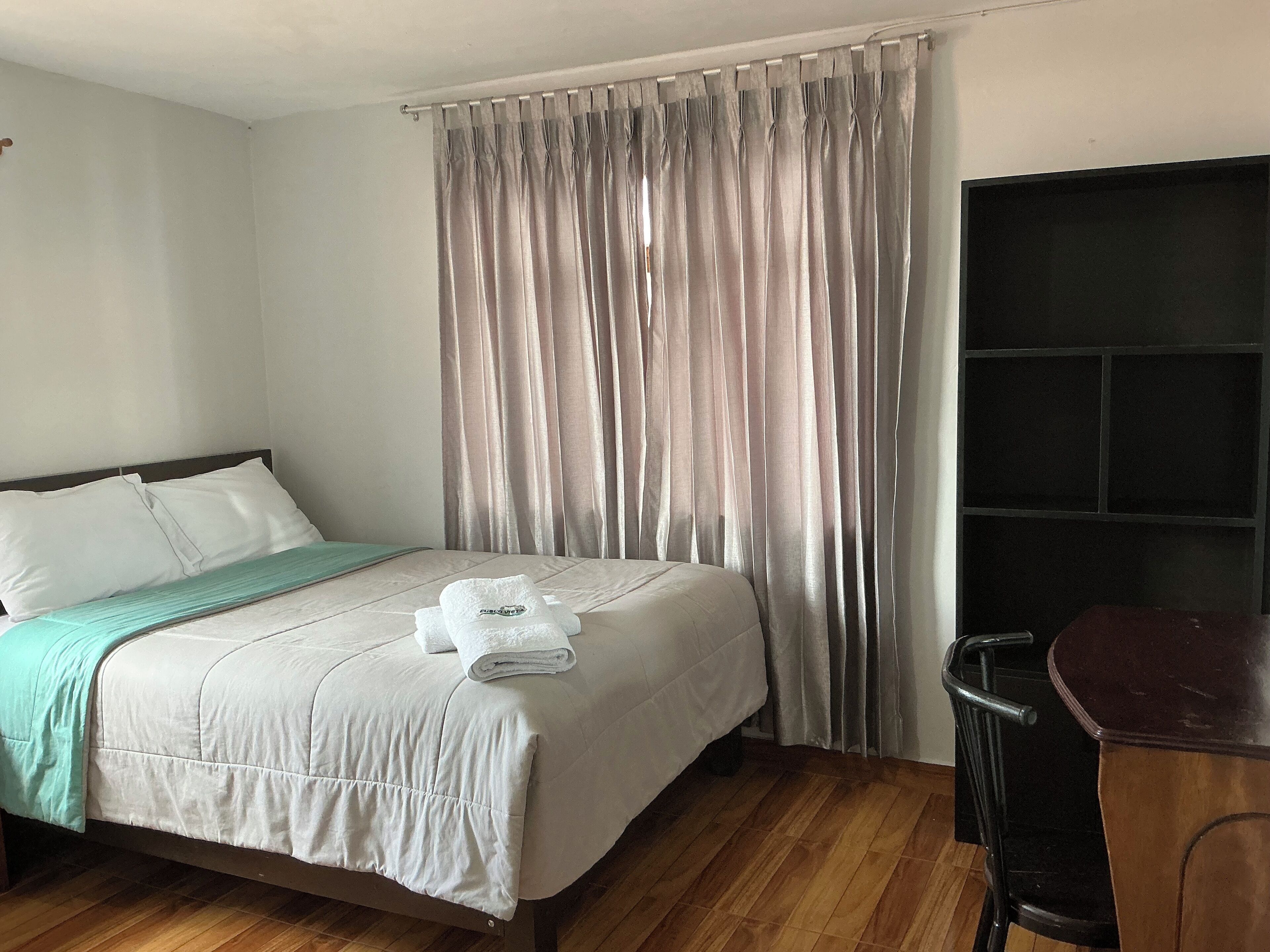 Een hotelkamer met een bed, een bureau en een groot raam met gordijnen.