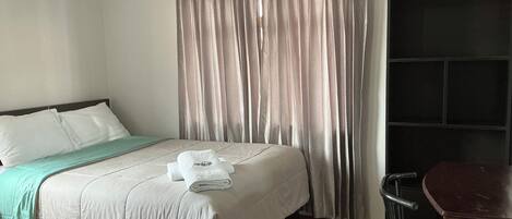 Ein Hotelzimmer mit Bett, Schreibtisch und einem großen Fenster mit Vorhängen.