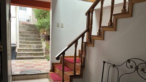 A staircase with wooden railings and red carpeted steps leading to an outdoor area with a stone wall and potted plants. - CUSCO VISTA GUETS HOUSE (Cusco)