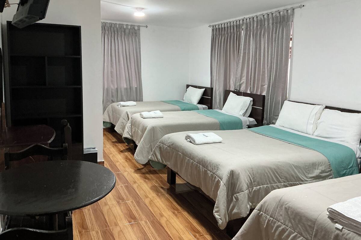 A hotel room with two single beds, a small table, and a chair.