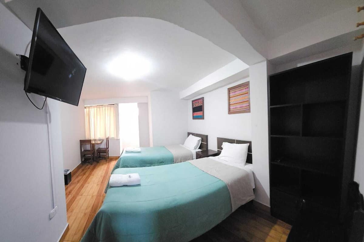 A hotel room with two beds, a TV, a desk, and a chair.