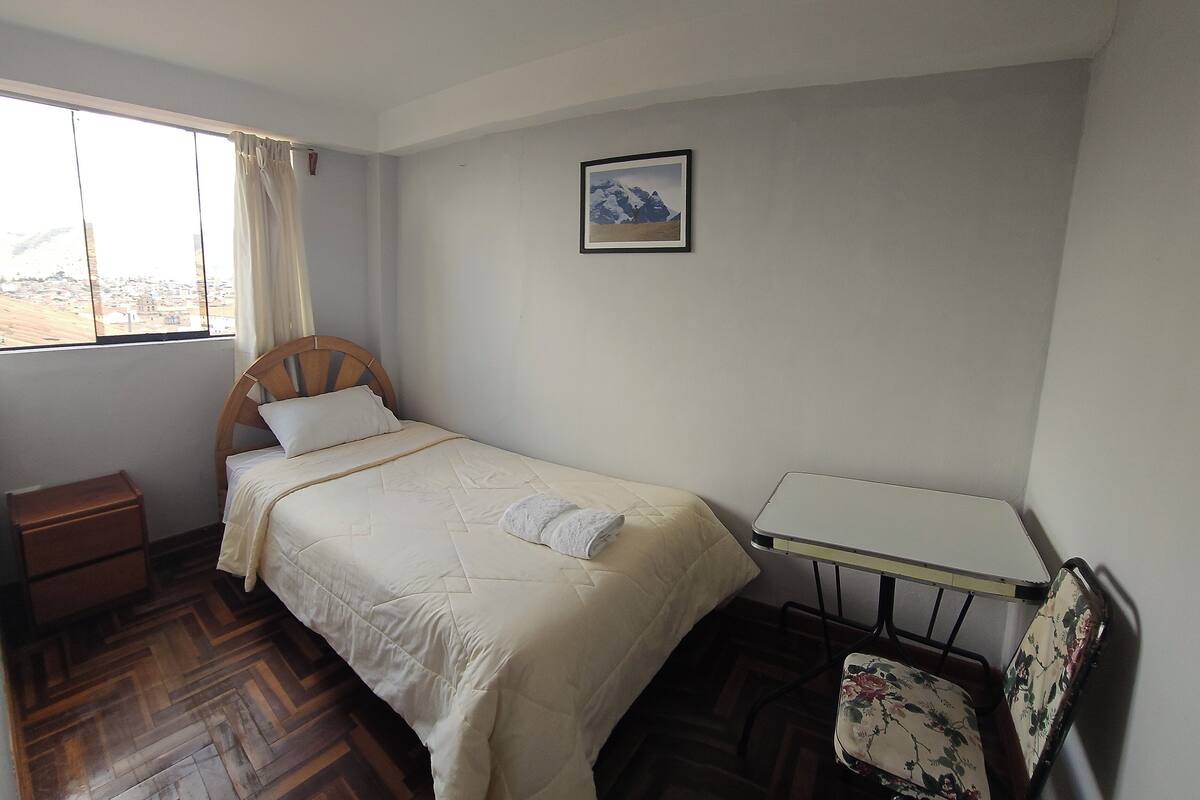 A bedroom with a bed, a small table, a chair, a nightstand, and a window with curtains.