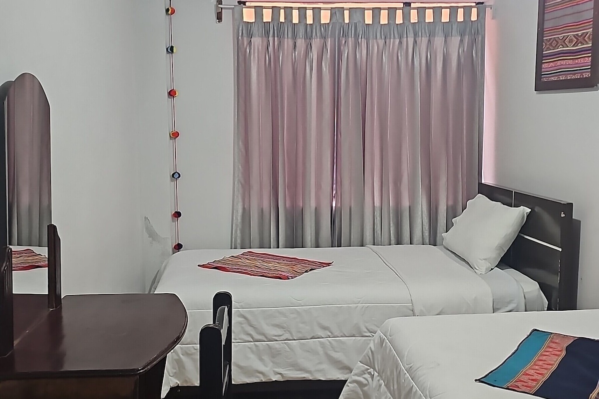 A hotel room with two beds, a wooden floor, a desk, and a ceiling light.