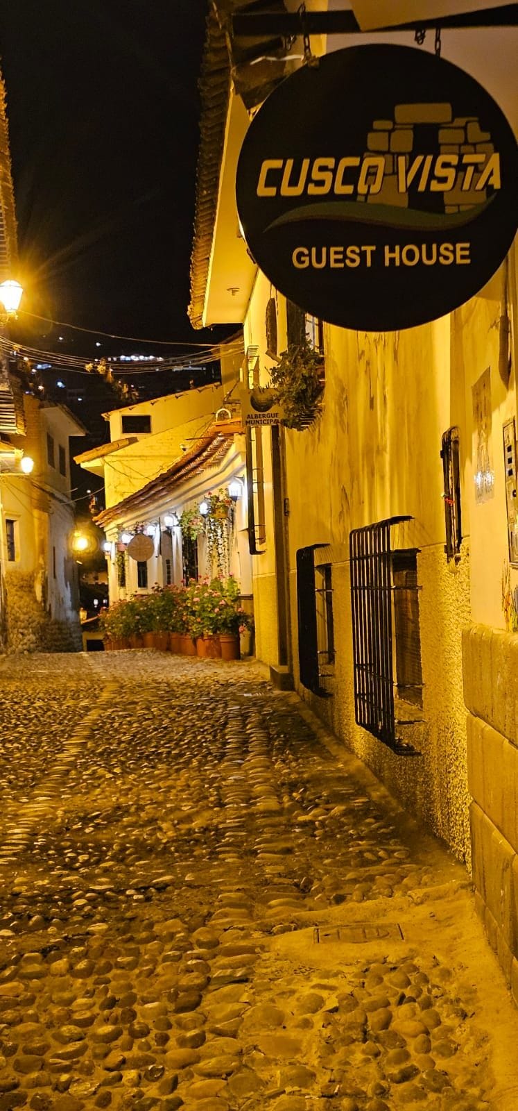 A cobblestone street leading to a building with a sign reading 'CUSCO VISTA GUEST HOUSE'.