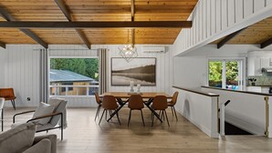 Una cocina moderna con armarios blancos, una mesa de comedor de madera y vistas a una casa a través de amplios ventanales.