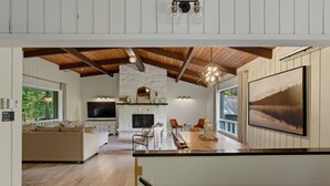 Amplia sala de estar con chimenea, televisor y comedor con un ventanal grande.