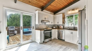 Una cocina moderna con gabinetes blancos, electrodomésticos de acero inoxidable y techo de madera.