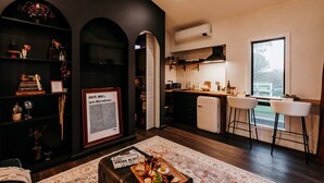 A modern kitchen with a built-in oven, a dining area with a bar stool, and a bookshelf with various items. - the tiny burrow ~ magical fleurieu escape (Aldinga)
