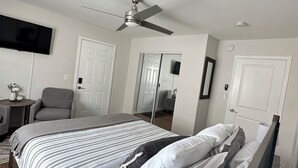 Un dormitorio con cama, ventilador de techo, televisor y una silla.