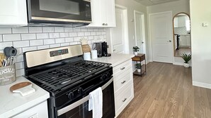 Una cocina moderna con armarios blancos, una campana extractora de acero inoxidable, una estufa negra y un salpicadero de azulejos.