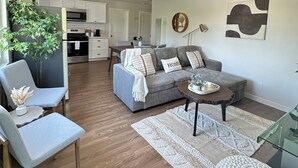 Una sala moderna con un sofá gris, una mesa de centro y un comedor al fondo.