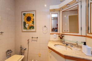 A bathroom with a sink, mirror, and a framed sunflower picture on the wall. - Copacabana com Varanda – 3 min da praia (Rio de Janeiro)
