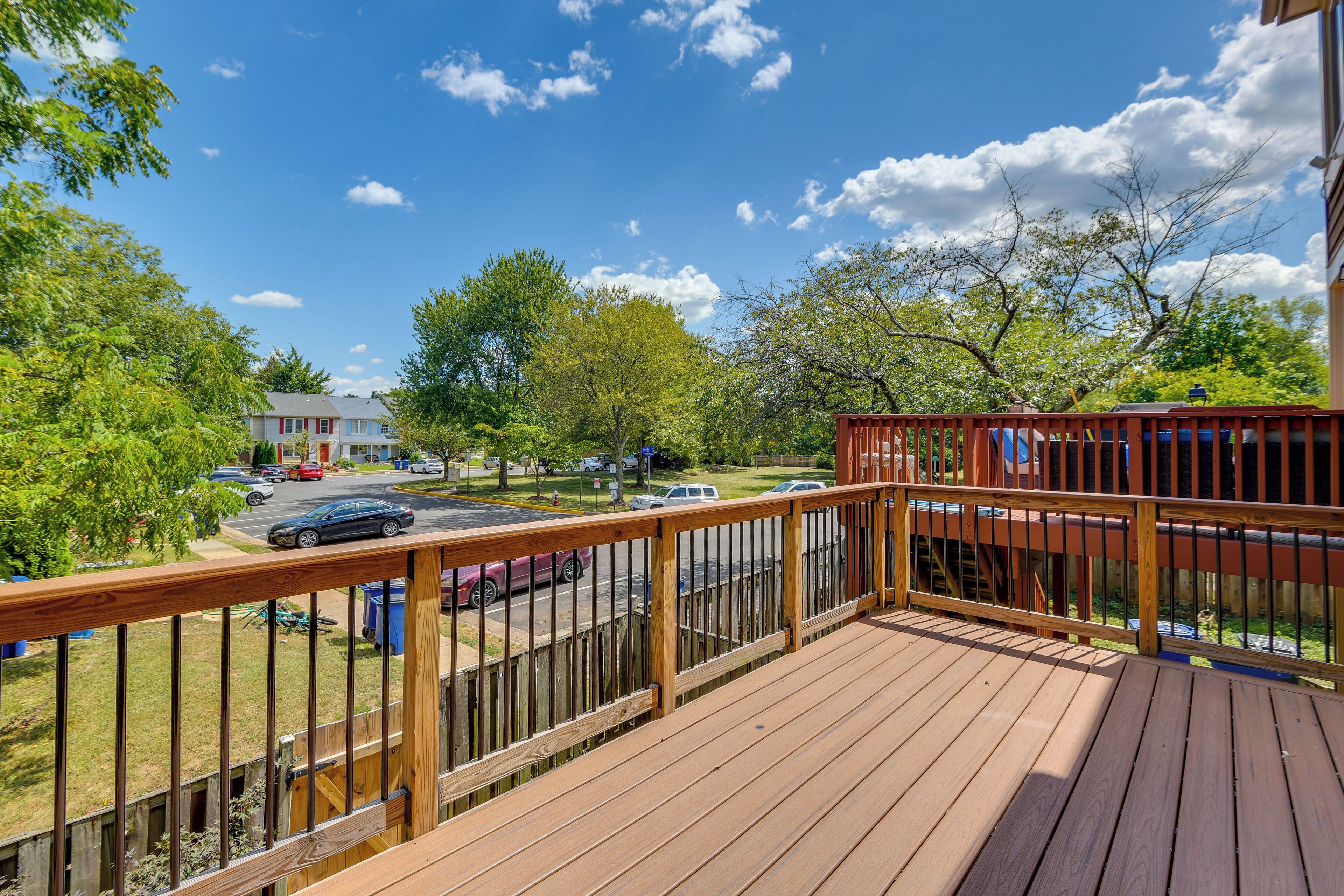 A wooden deck with a railing overlooking a street with parked cars and trees.