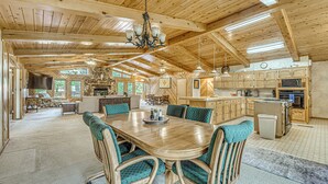 Un intérieur spacieux en bois, avec une grande table à manger entourée de chaises, un coin cuisine et une cheminée.