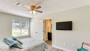 Ein Schlafzimmer mit einem Bett, einem Deckenventilator, einem an der Wand montierten Fernseher und einem Fenster mit Jalousien.