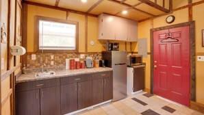 Una cocina con alacenas de madera oscura, un refrigerador de acero inoxidable, un microondas y una puerta roja.