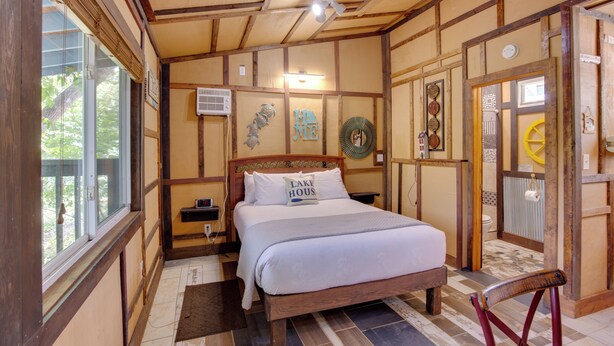 Un dormitorio con estructura de madera, una cama, una mesita de noche, una ventana y una puerta.