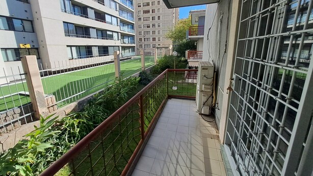 A balcony with a view of a sports field, surrounded by buildings.