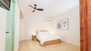 A bedroom with a bed, bedside lamps, a ceiling fan, and wall art. - Sunny Seaside Getaway (San Juan)