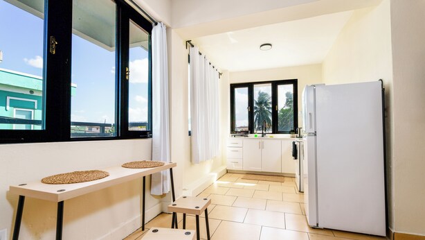 A compact kitchen with a refrigerator, a dining table with stools, and a window with curtains. - Sunny Seaside Getaway (San Juan)