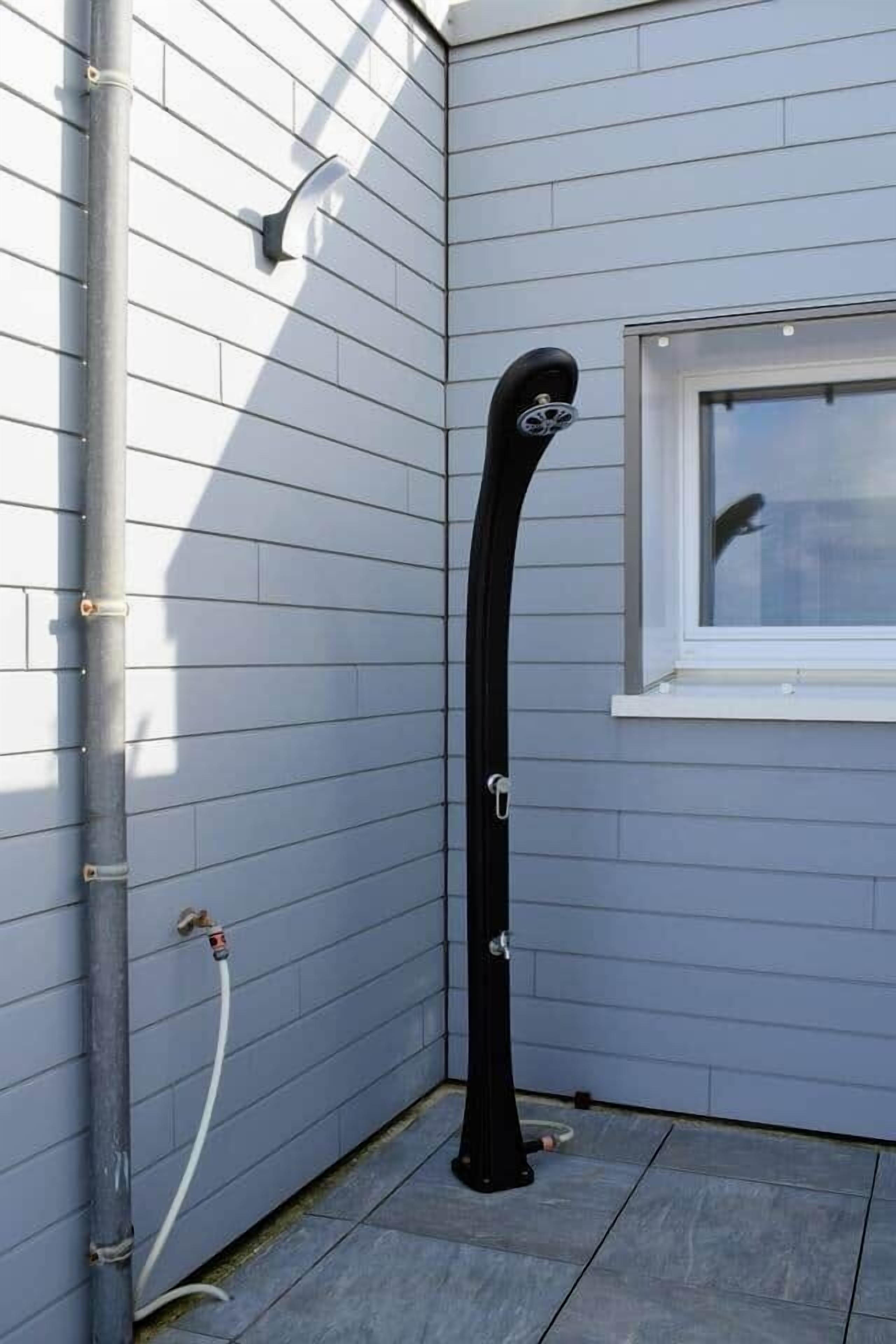 A black outdoor water feature with a curved design, positioned against a light gray wall with a window.