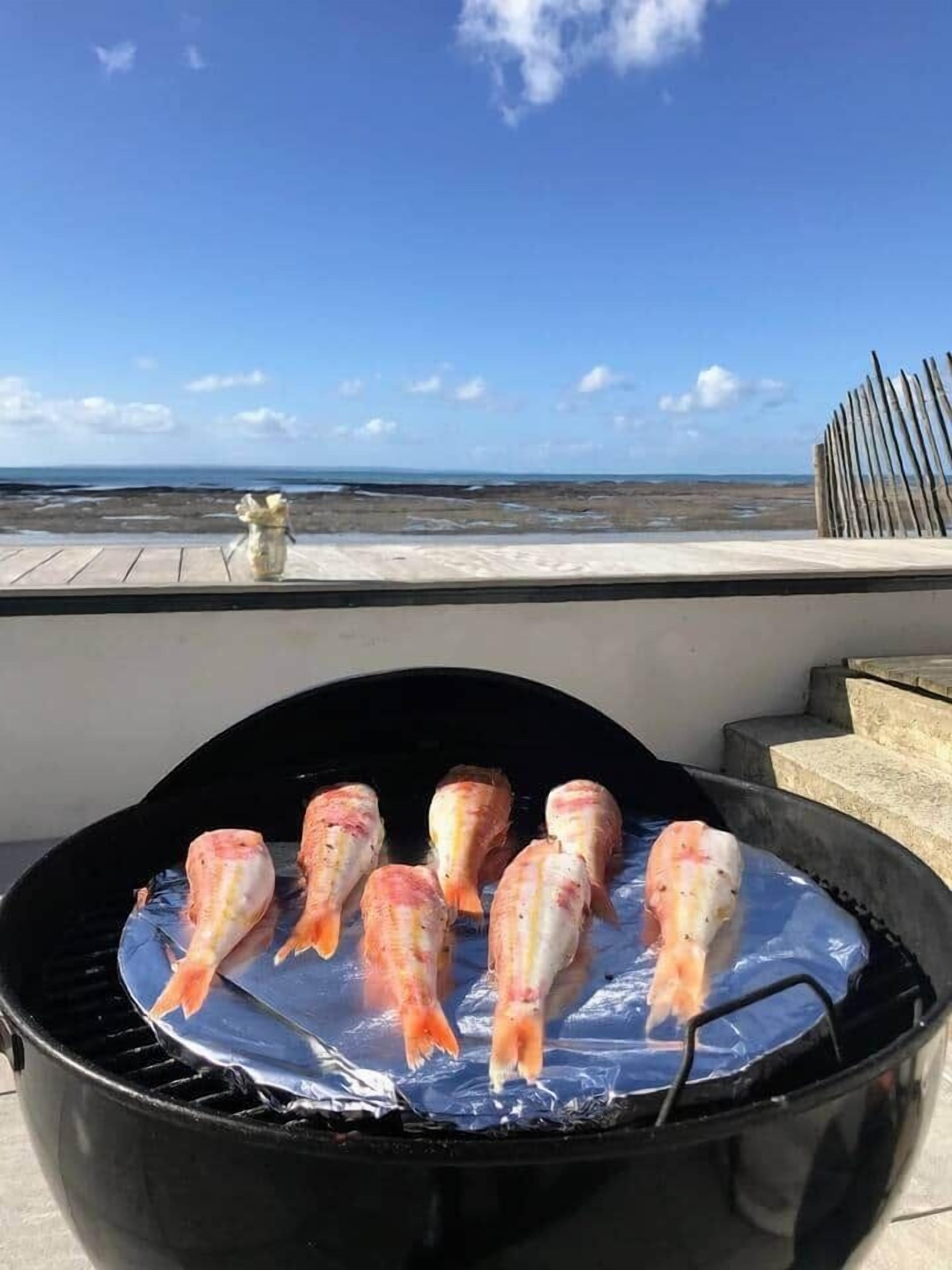 Ein Grill mit Fisch auf einem Balkon mit Blick auf einen Strand.