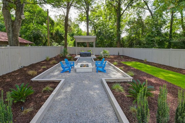 A backyard with a fire pit, two blue chairs, and a covered seating area.