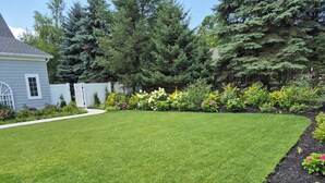 A well-maintained lawn with a variety of flowering plants and shrubs, a white fence, and a house with a grey exterior. - Cozy studio in Douglas with swimming pool and fireplace. (Douglas)
