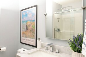 Ein Badezimmer mit einem gerahmten Gemälde von Claude Monet, einer modernen Dusche und einem Topf Lavendel.