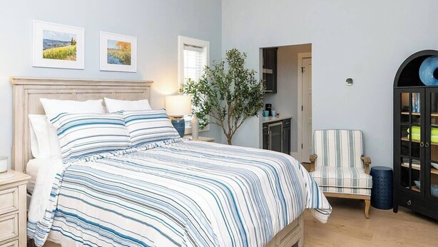 A bedroom with a bed, nightstands, a chair, a cabinet, and two framed pictures on the wall. - Cozy studio in Douglas with swimming pool and fireplace. (Douglas)