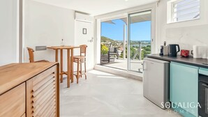 A modern kitchen with a view of the sea, a dining area with a table and chairs, and a sliding glass door leading to an outdoor seating area.