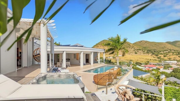 A modern outdoor pool area with lounge chairs and a hot tub, surrounded by a landscaped garden and a view of the hills.