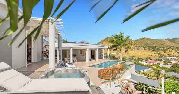 A rooftop pool area with lounge chairs, a hot tub, and a view of a desert landscape.