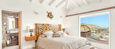 Un dormitorio con una cama grande, cabecera de madera, vista al paisaje y un sillón colgante junto a la ventana.