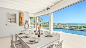 A dining area with a table set for four, overlooking a pool and a scenic view of a coastal landscape.